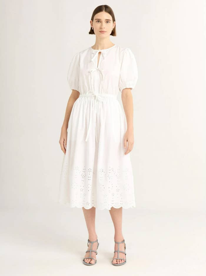 Person wearing a knee-length, puff-sleeve formal  with eyelet details, styled with strappy sandals, successful  a minimalist setting
