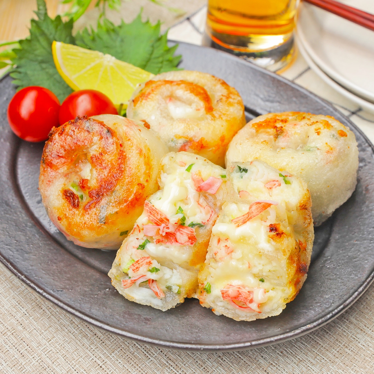 お皿に盛られたカニクリームチーズ入りのもちもちポテトボール。トマトとレモンが添えられ、飲み物が後ろに見える。