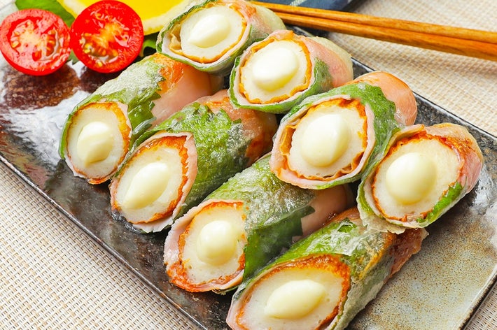 盛り付けたチーズと魚肉を使った春巻きが皿に並び、横には半分に切ったプチトマトとレモンが添えられています。