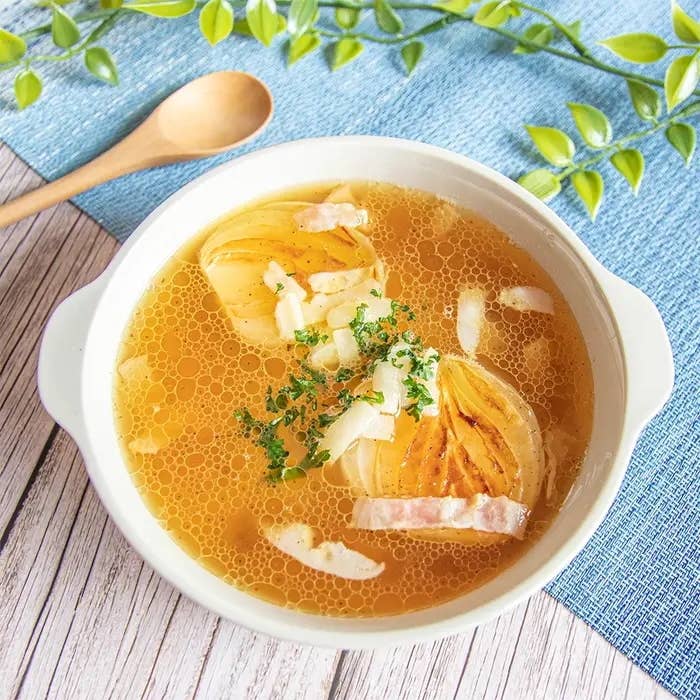 スープ皿に盛られた玉ねぎスープ。玉ねぎとベーコンが浮かび、ハーブが散らされています。木製スプーンが横に置かれています。