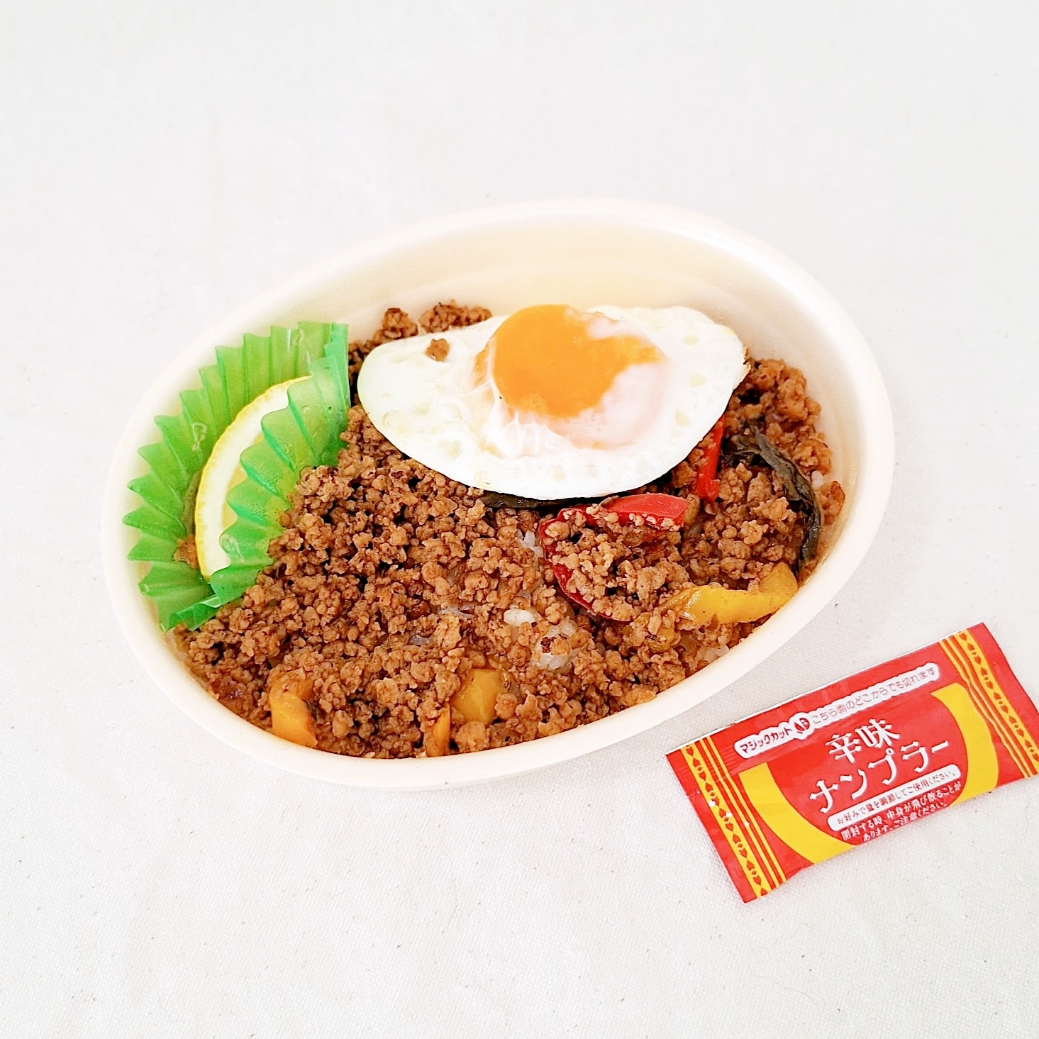 目玉焼きとひき肉が載った弁当。隣に調味料の袋があります。