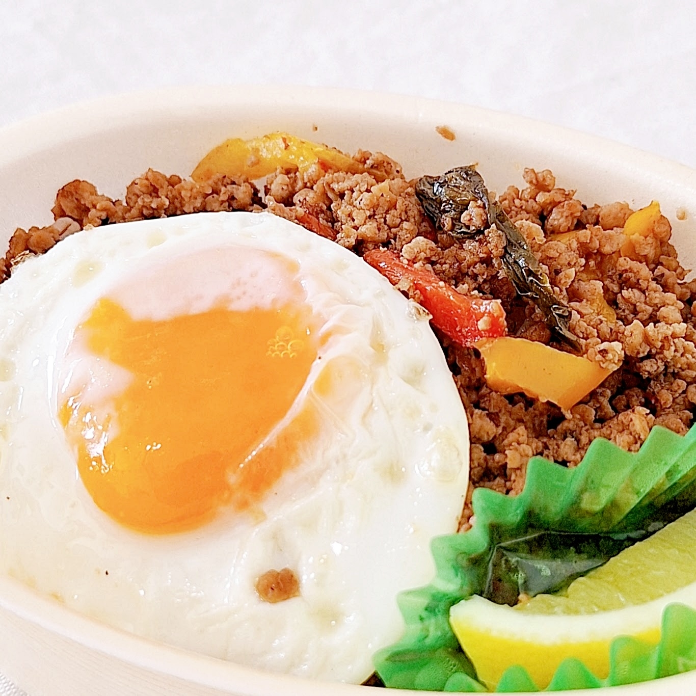 目玉焼きが乗ったピリ辛ひき肉と野菜の弁当。レモンとグリーンの仕切り付き。