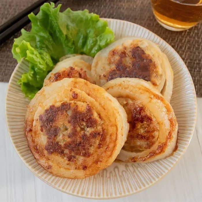 お皿に盛られた玉ねぎ料理とサラダ菜。背景に器と箸が見える。