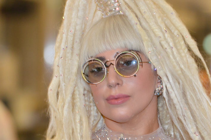 セレブが独特なスタイルの長いドレッドヘアと丸いメガネをかけている。ビーズと花柄の装飾が施されたドレスを着ている。