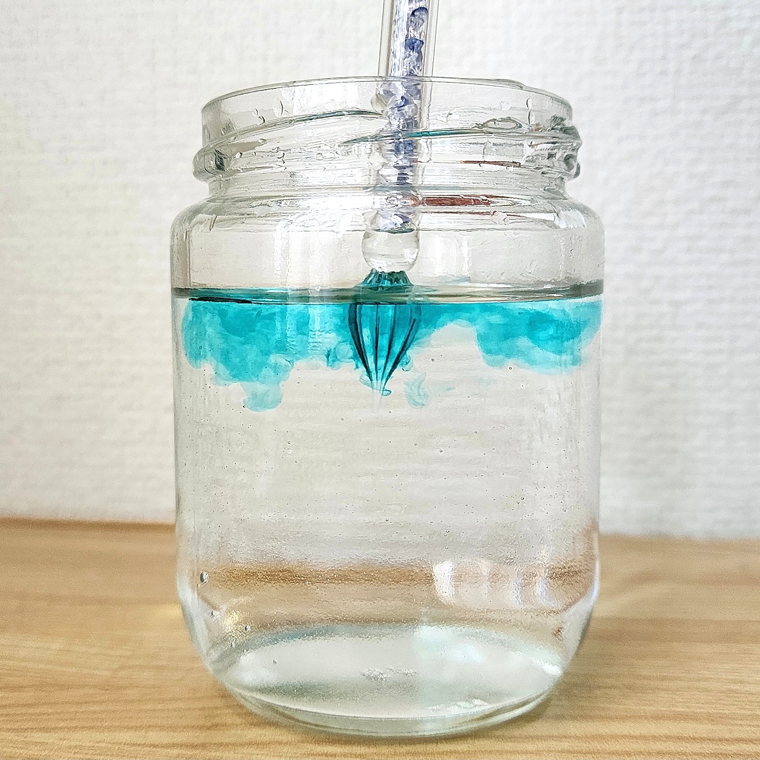 ガラス瓶に水が入っており、青のインクが上から垂れ落ちて広がっている様子。