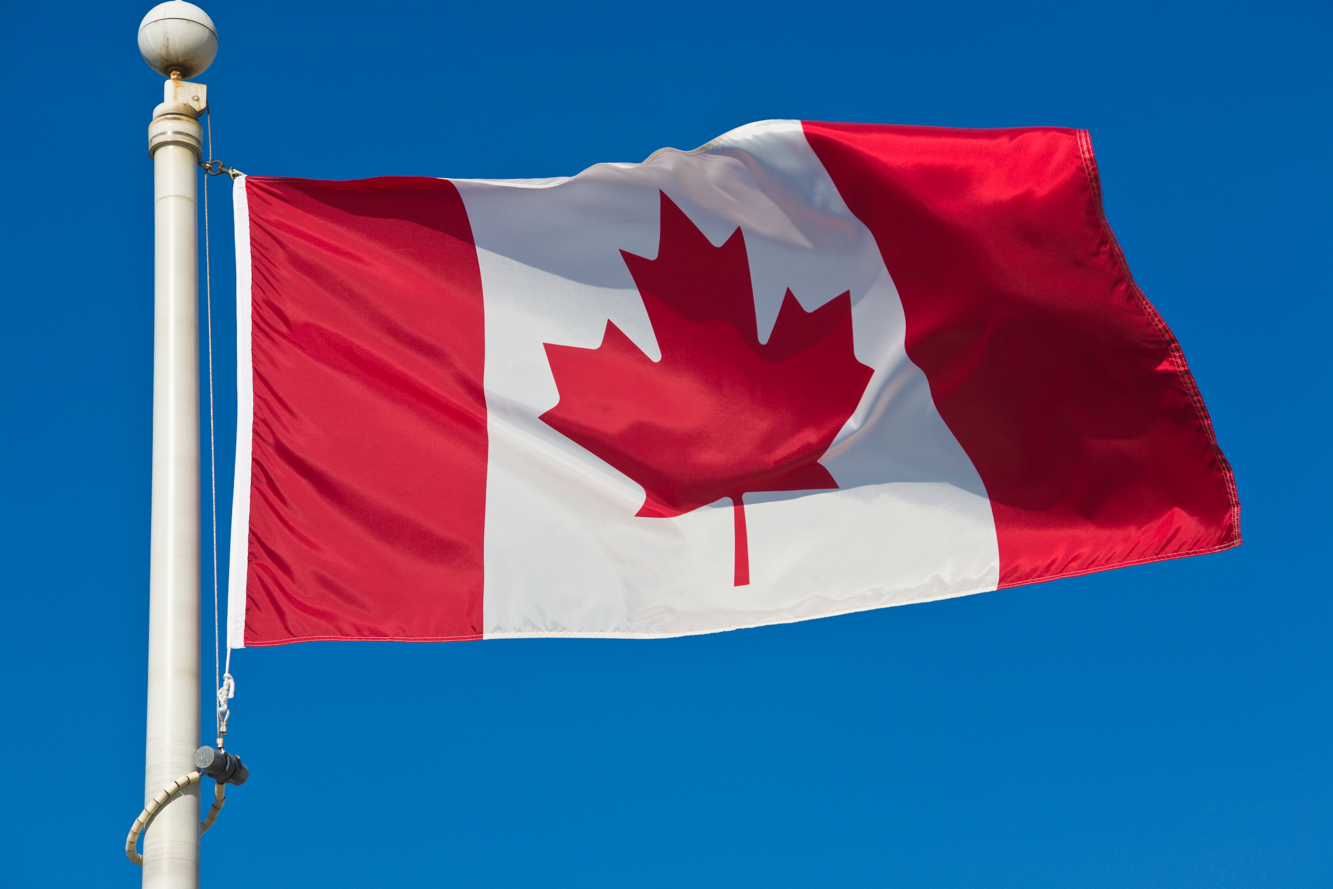 Canadian flag waving on a flagpole against a clear blue sky