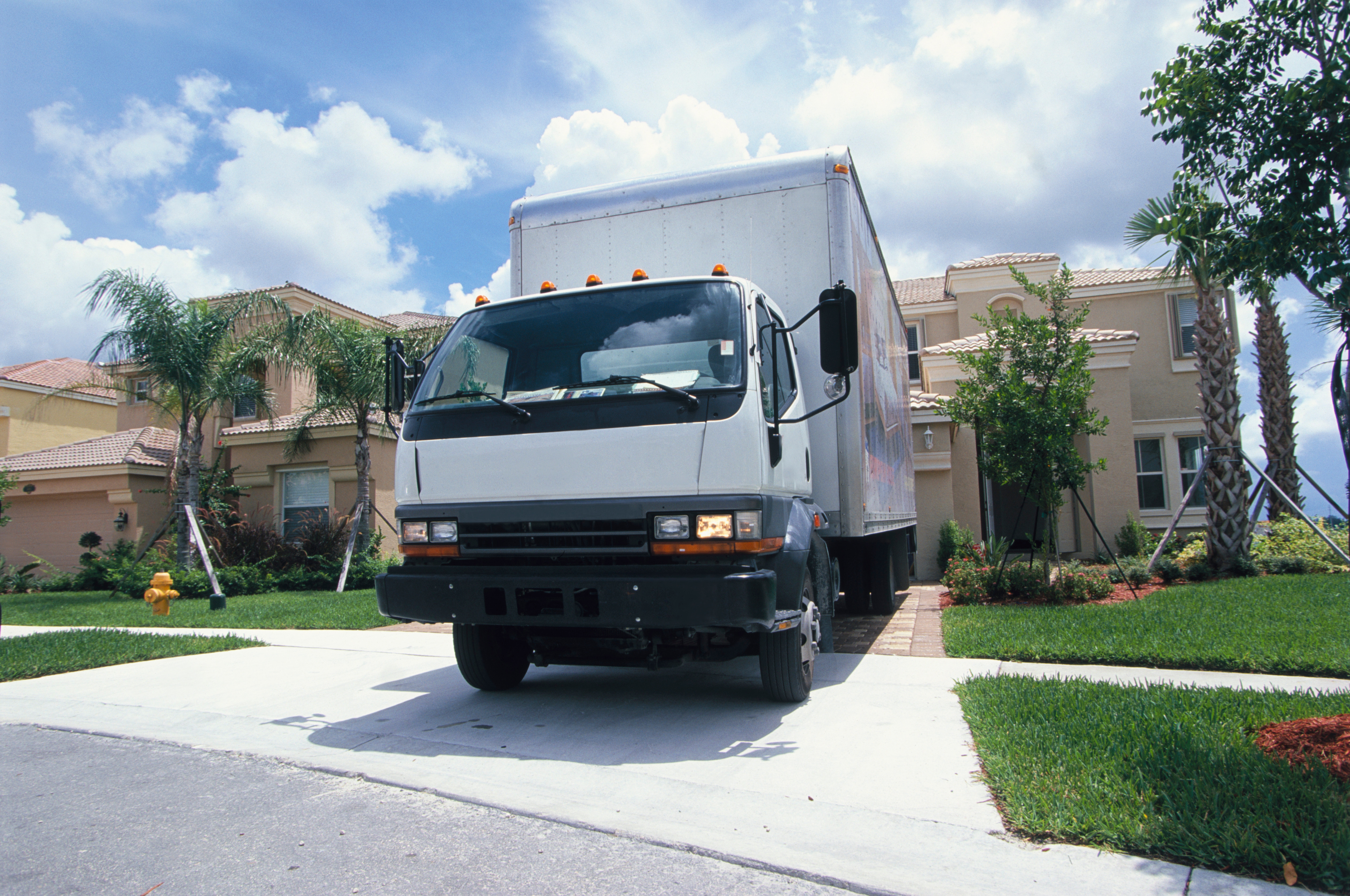 A moving truck is parked in the driveway of a suburban house surrounded by palm trees
