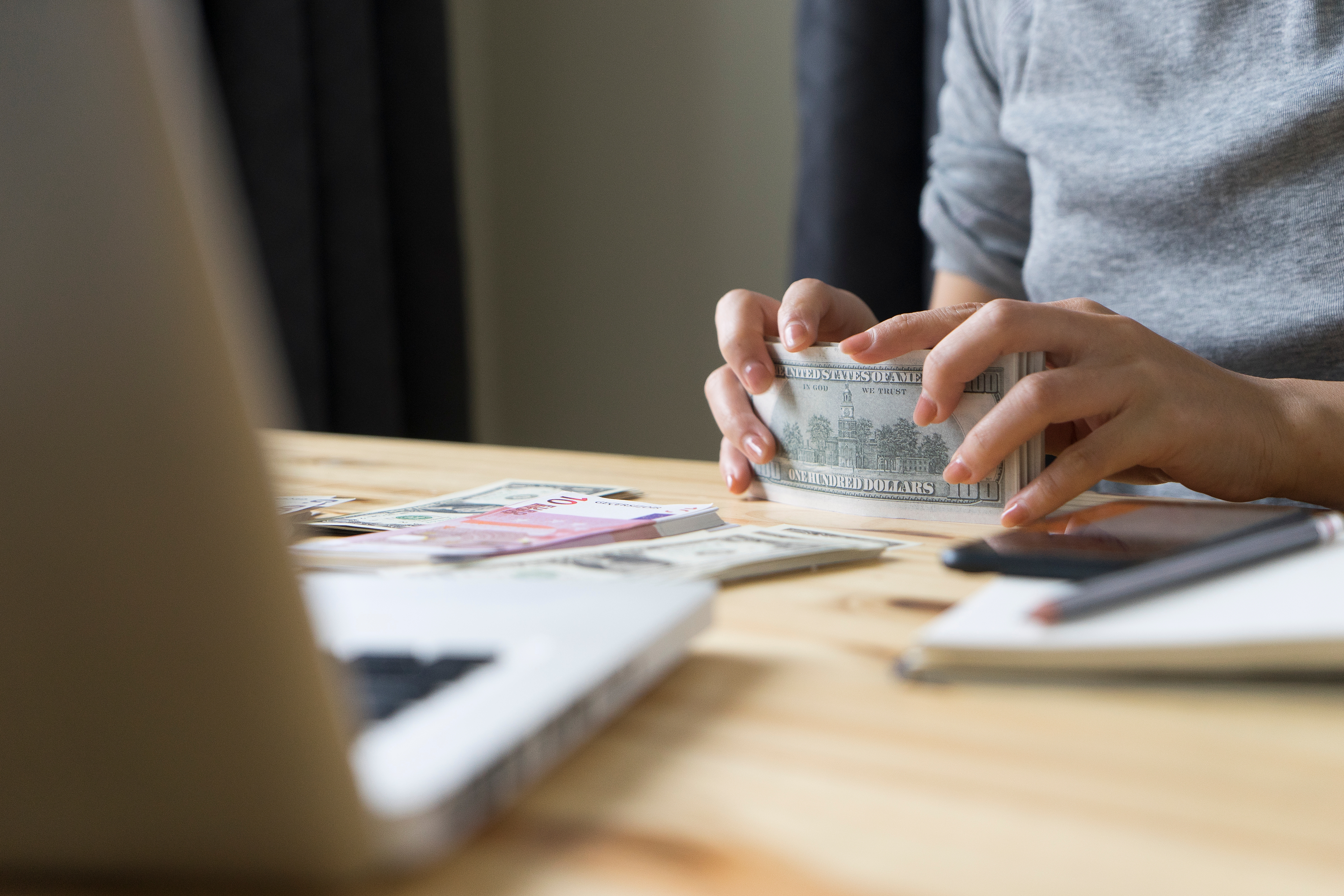 Person counting money at a desk with a laptop and notepad, suggesting financial planning or budgeting