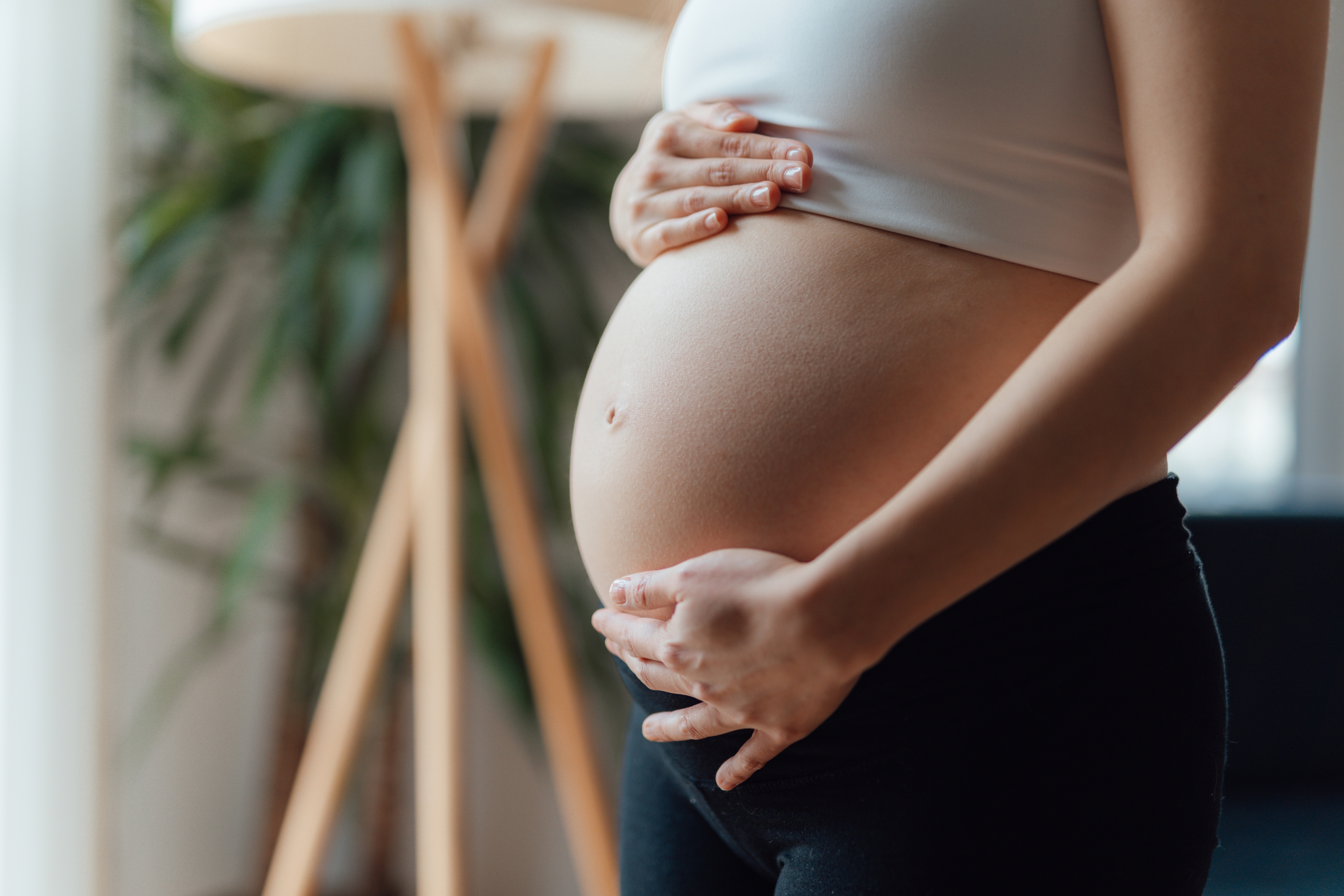 Pregnant person gently cradling their belly, standing indoors, conveying themes of love and anticipation