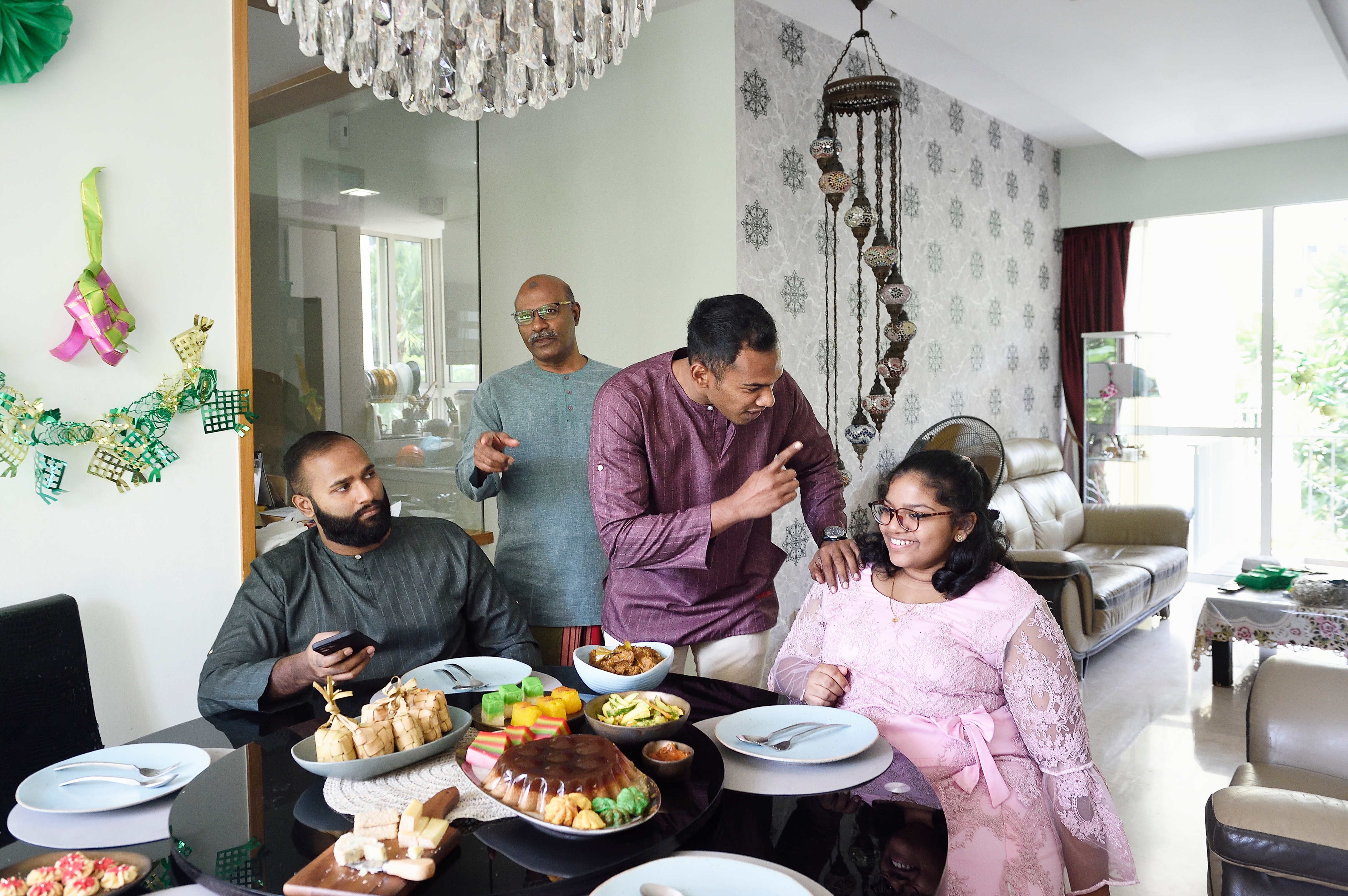 Family gathered around a dining table, engaged in conversation and sharing a meal. The room is decorated with wall art and a chandelier
