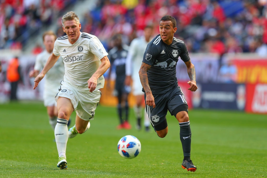 Two soccer players intensely chase a ball during a match. The player on the left wears a light-colored uniform, while the player on the right wears a dark uniform