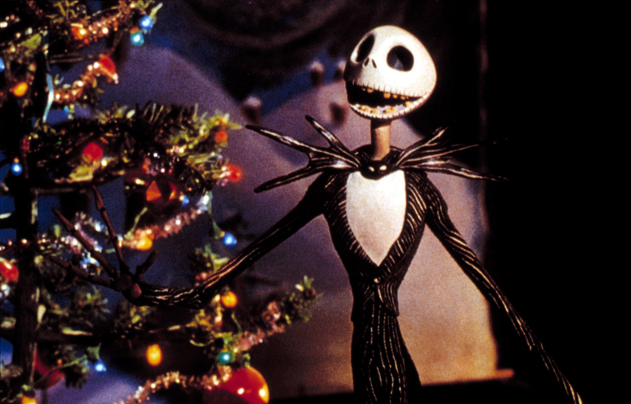 Jack Skellington stands by a decorated Christmas tree, dressed in his iconic pinstripe suit from "The Nightmare Before Christmas."
