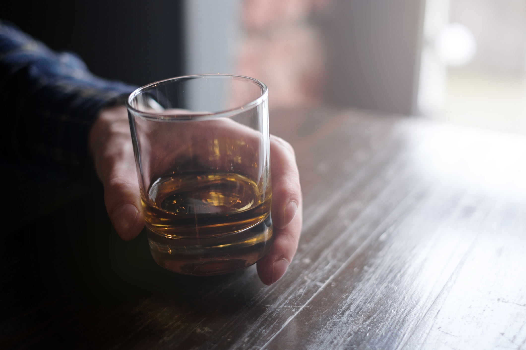 Person som holder et glass whisky på et trebord, og skaper en avslappet atmosfære