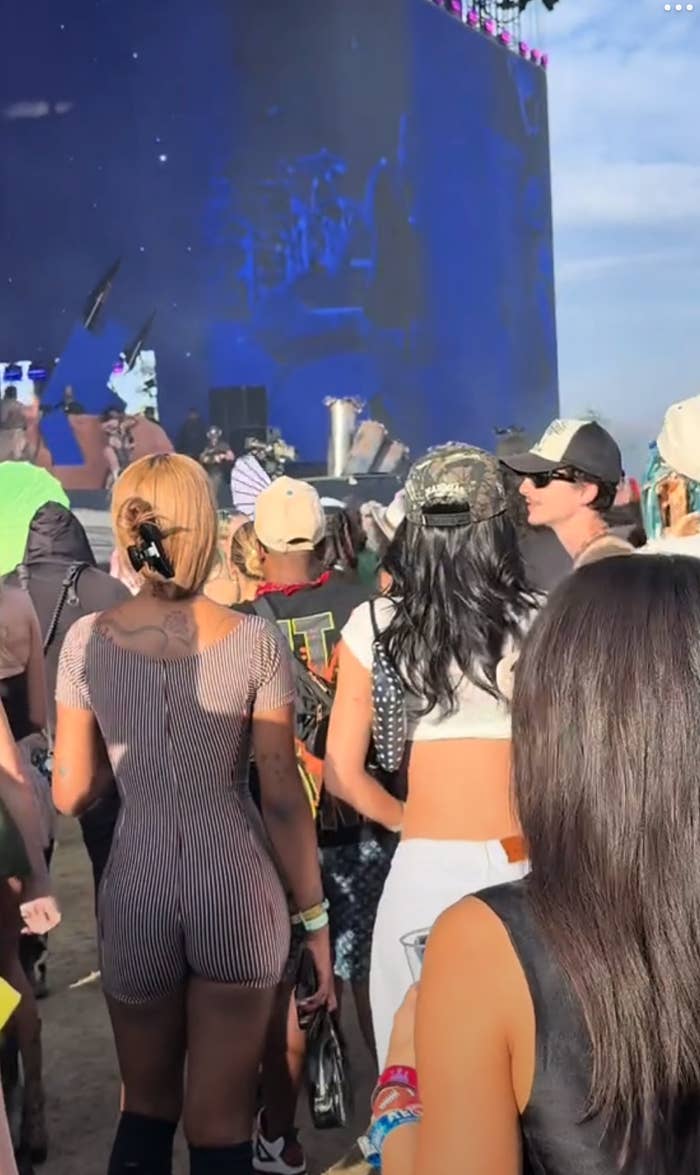 People at a lively outdoor event watch a stage performance, dressed in casual and stylish festival attire