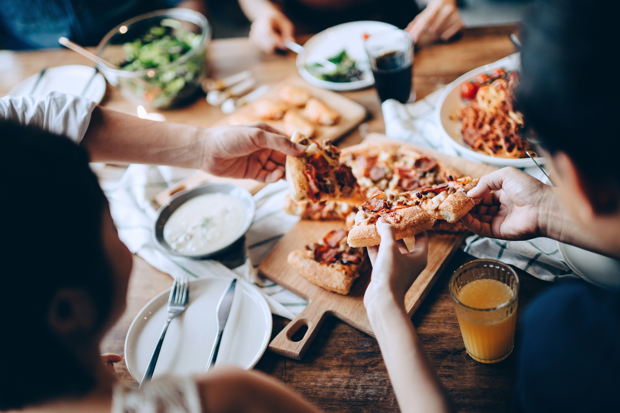 Folk som deler pizzakiver ved et spisebord sett med retter, drikke og en salat