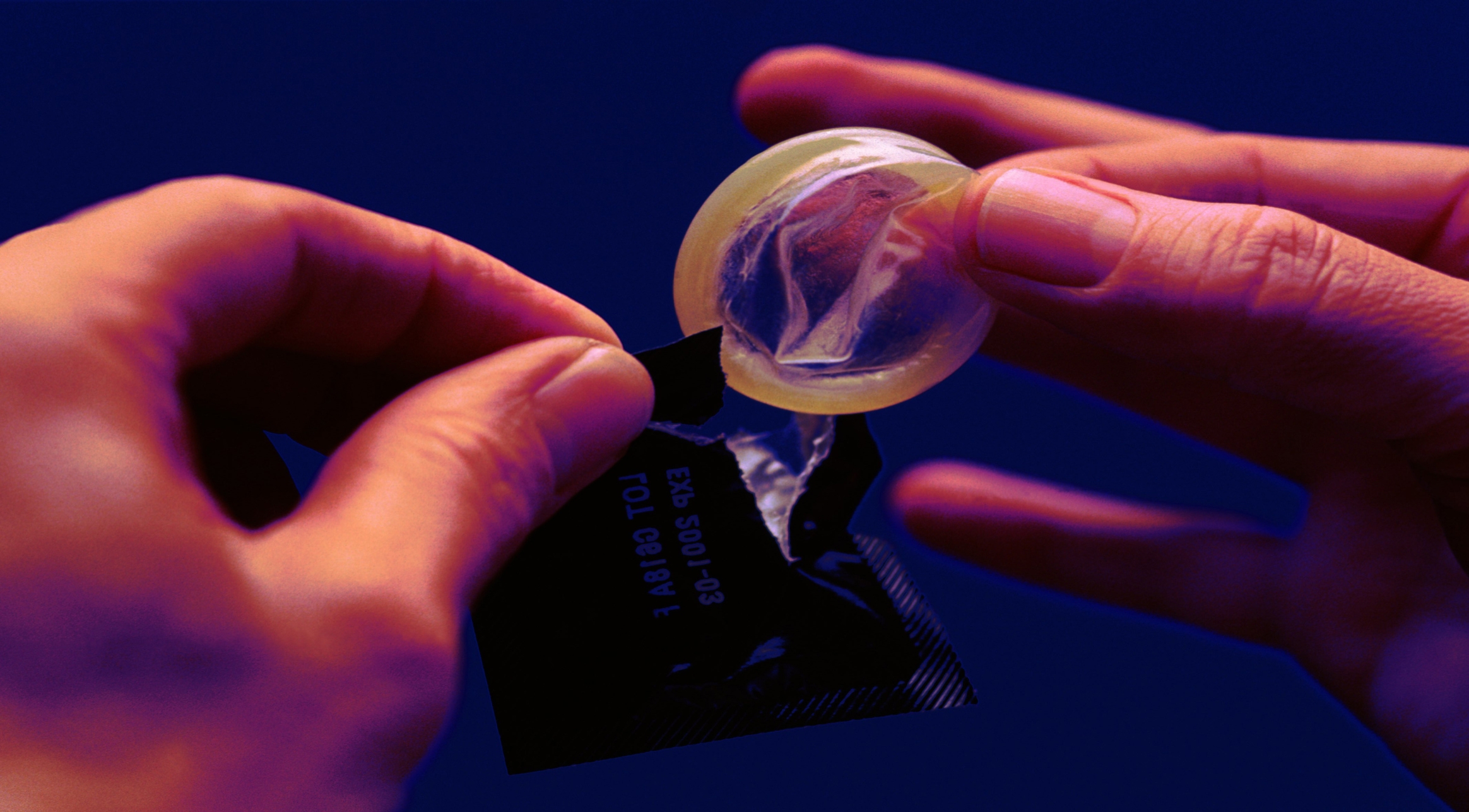 Person opening a condom packet and holding the condom, emphasizing safe practices