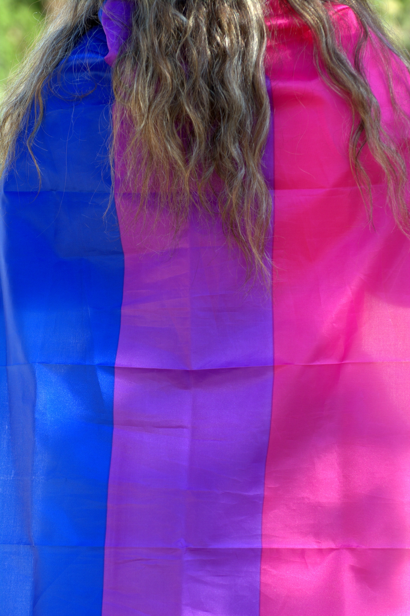 Person with wavy hair draped in a bisexual pride flag, featuring blue, purple, and pink stripes
