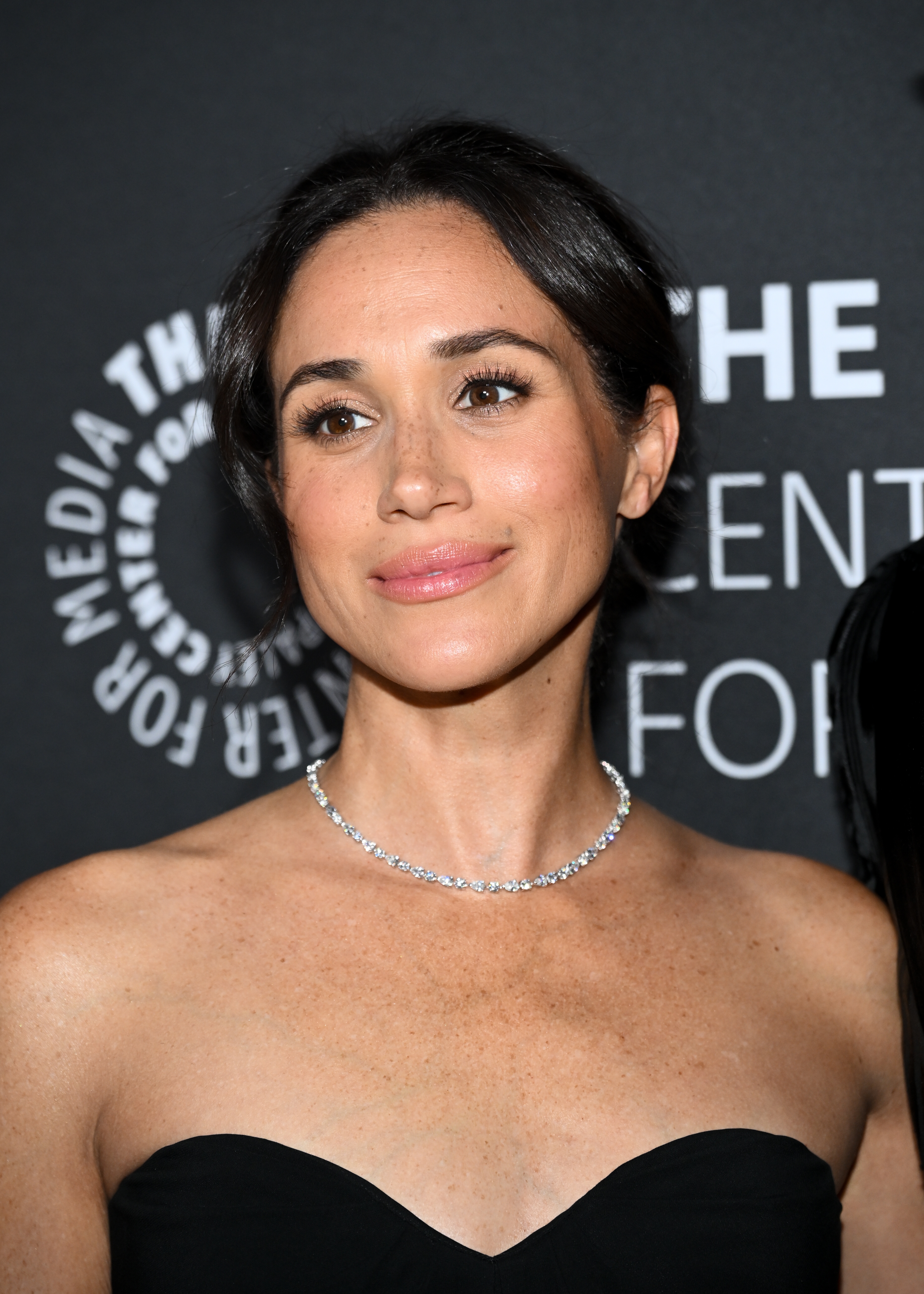 Meghan Markle in strapless gown and necklace at event backdrop