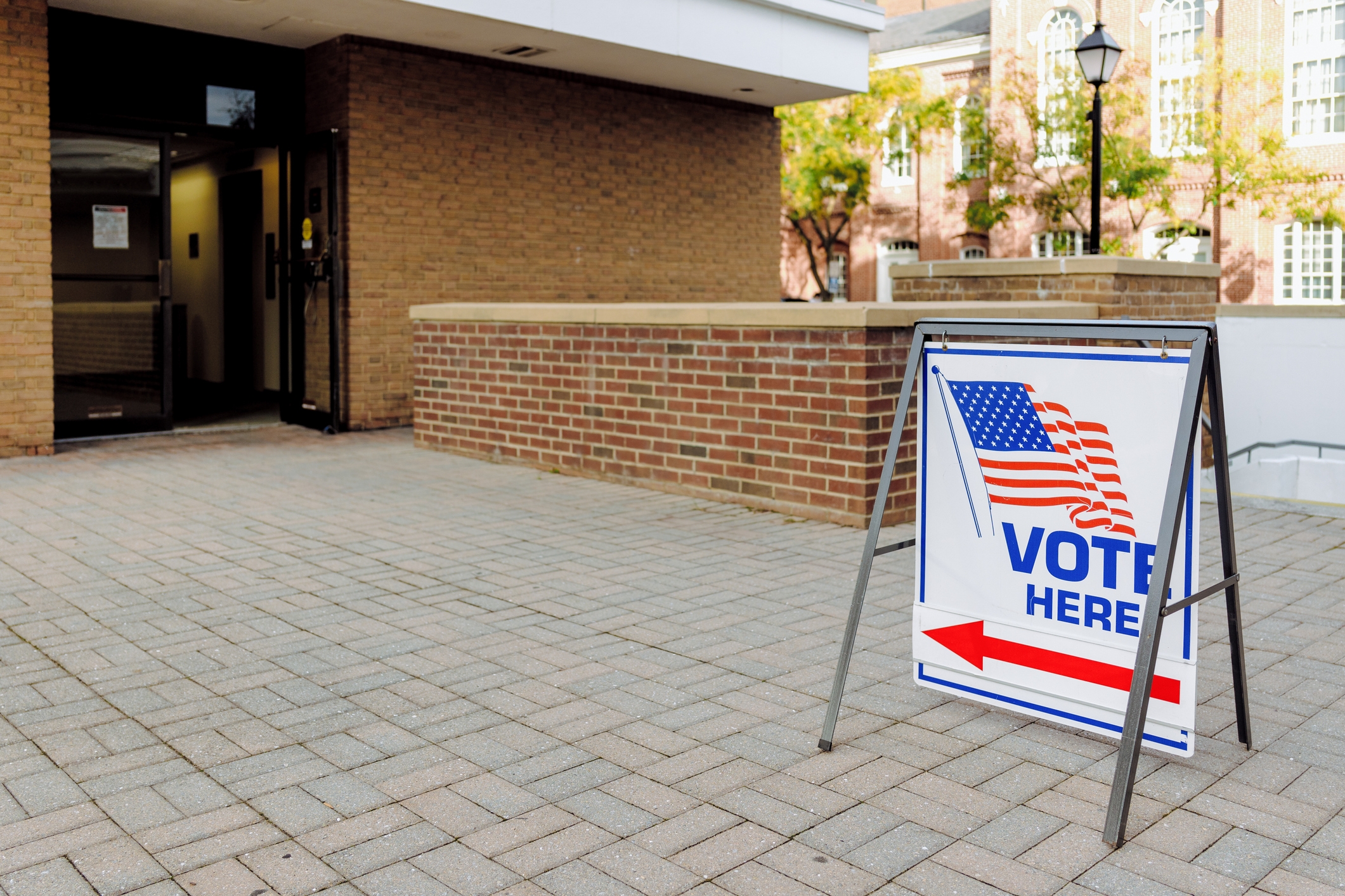 "Vote Here" sign with an arrow, displayed at the entrance of a brick building, indicating a polling location
