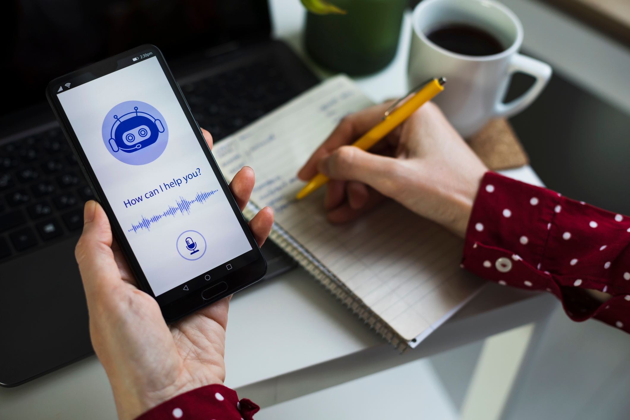 Person holds smartphone with digital assistant AI app open, while writing in a notebook