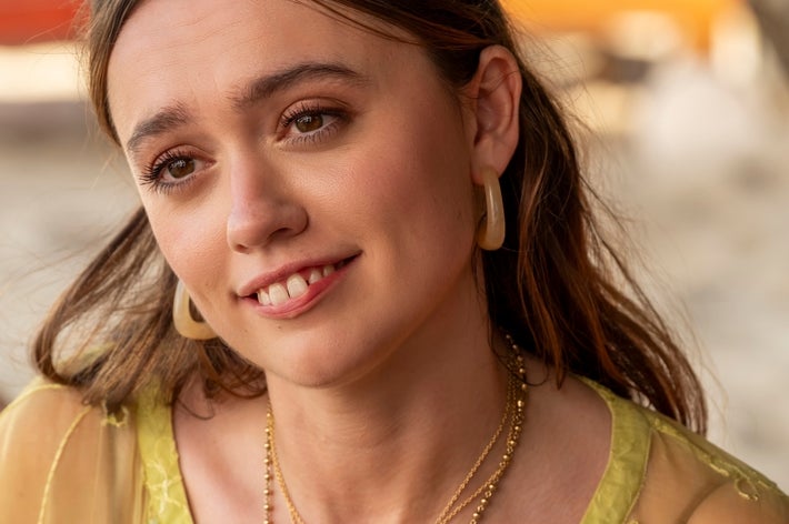 Person outdoors wearing a sheer top and layered necklaces, smiling gently