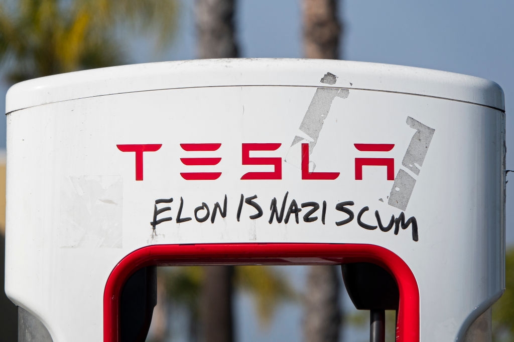 Tesla charging station with graffiti text reading "Elon is Nazi scum" on it