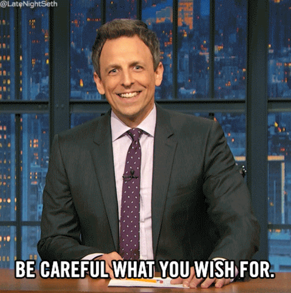 A person in a suit smiles while seated at a desk with the text "Be Careful What You Wish For" overlaid, implying anticipation or caution