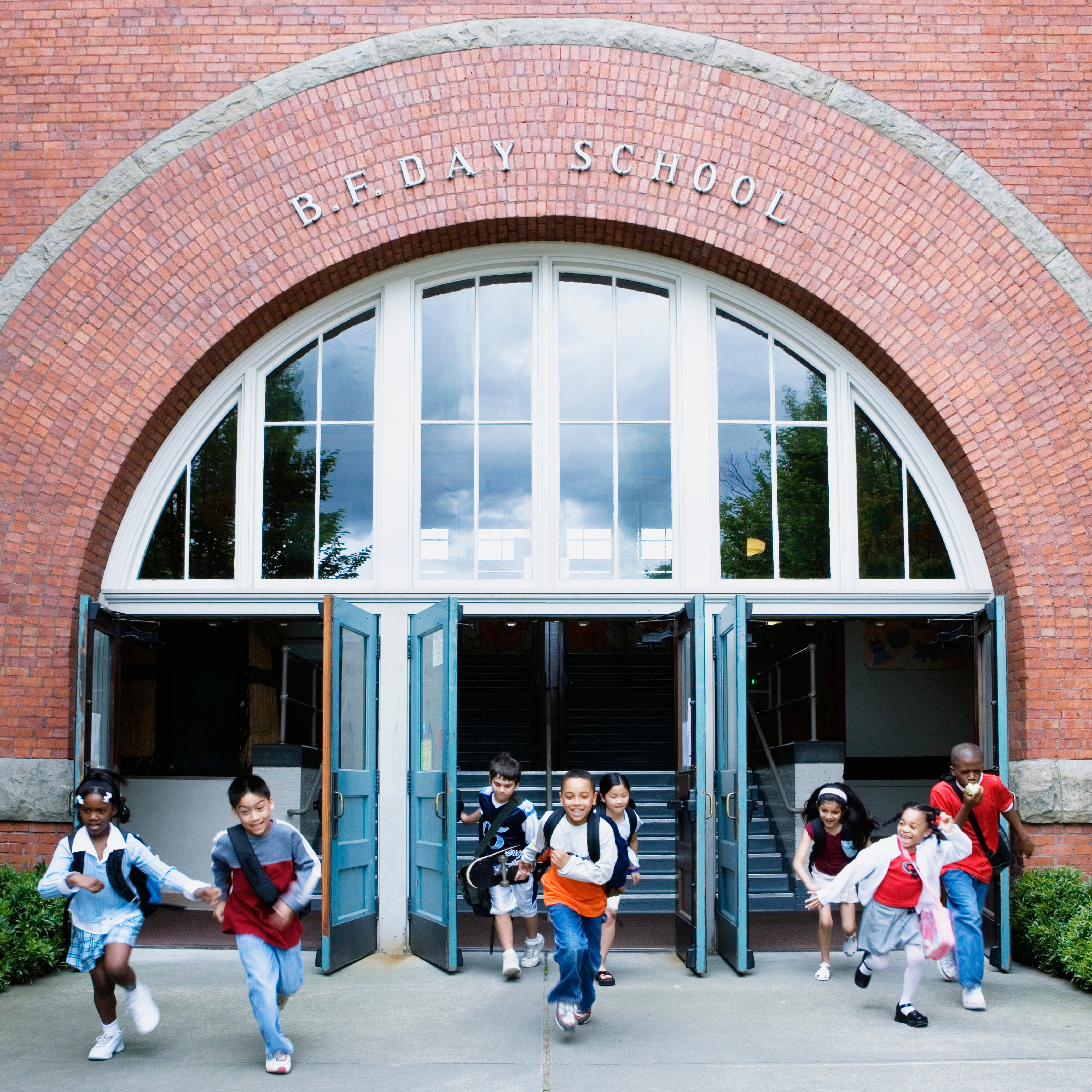 Children energetically run from a school building with wide, arched windows