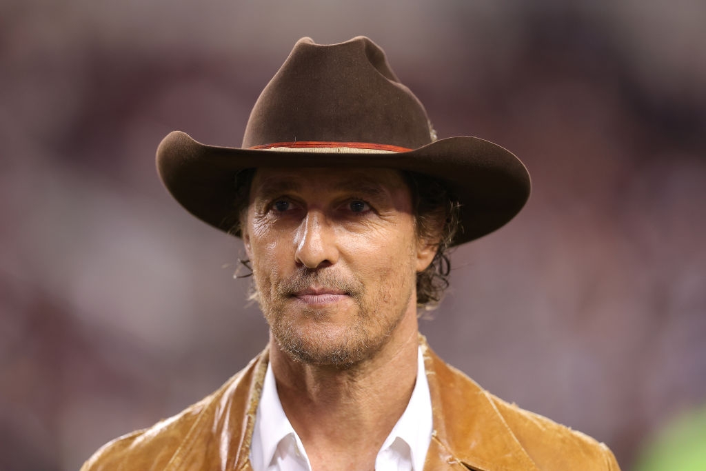 Man in a cowboy hat and suede jacket at an event, looking ahead with a neutral expression