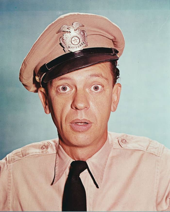 Person in a police uniform with a surprised expression, featuring a cap marked &quot;Mayberry.&quot;