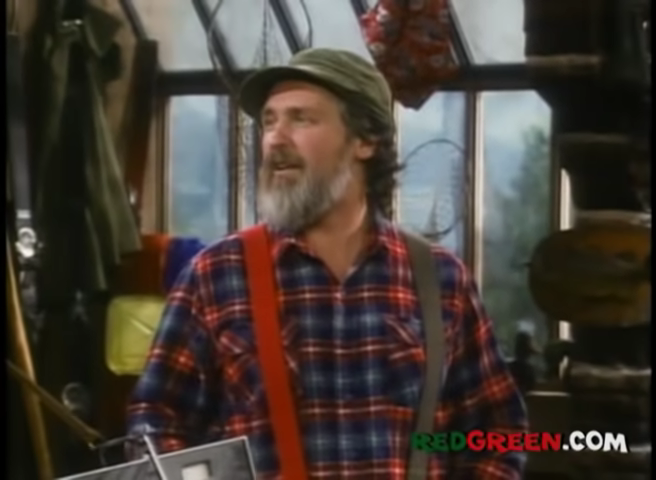 Person wearing a plaid shirt, suspenders, and a cap in what appears to be a rustic setting