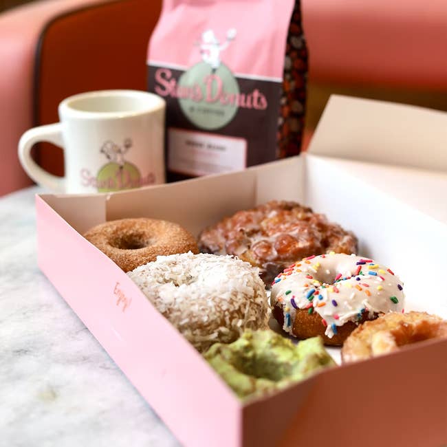 Box of assorted donuts with assorted toppings connected a table, accompanied by a java mug and a branded donut container successful the background
