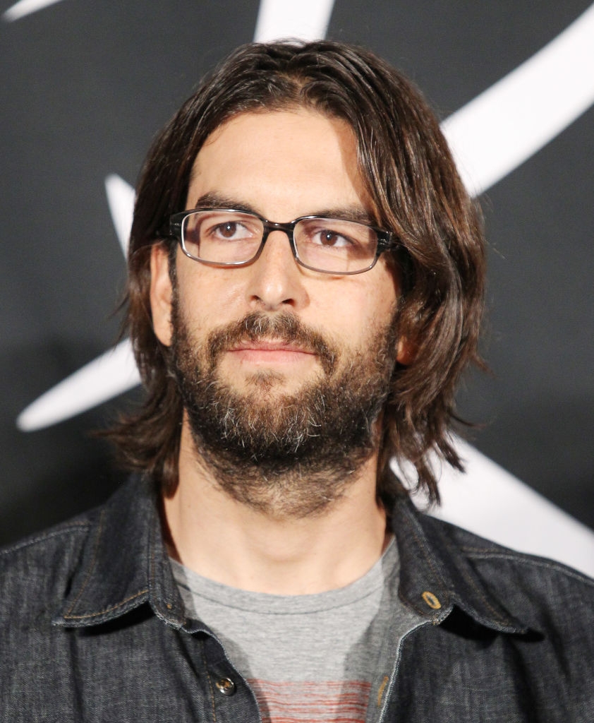 A person with glasses and long hair wearing a casual jacket at a public event