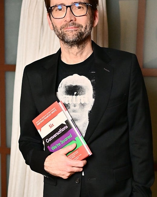 Man in black suit holding books, standing indoors