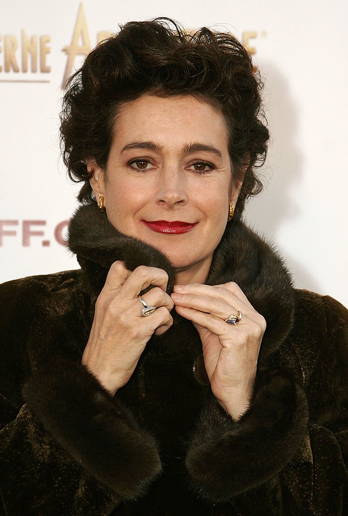Person in a dark fur coat, holding the collar, posing on a red carpet at an event