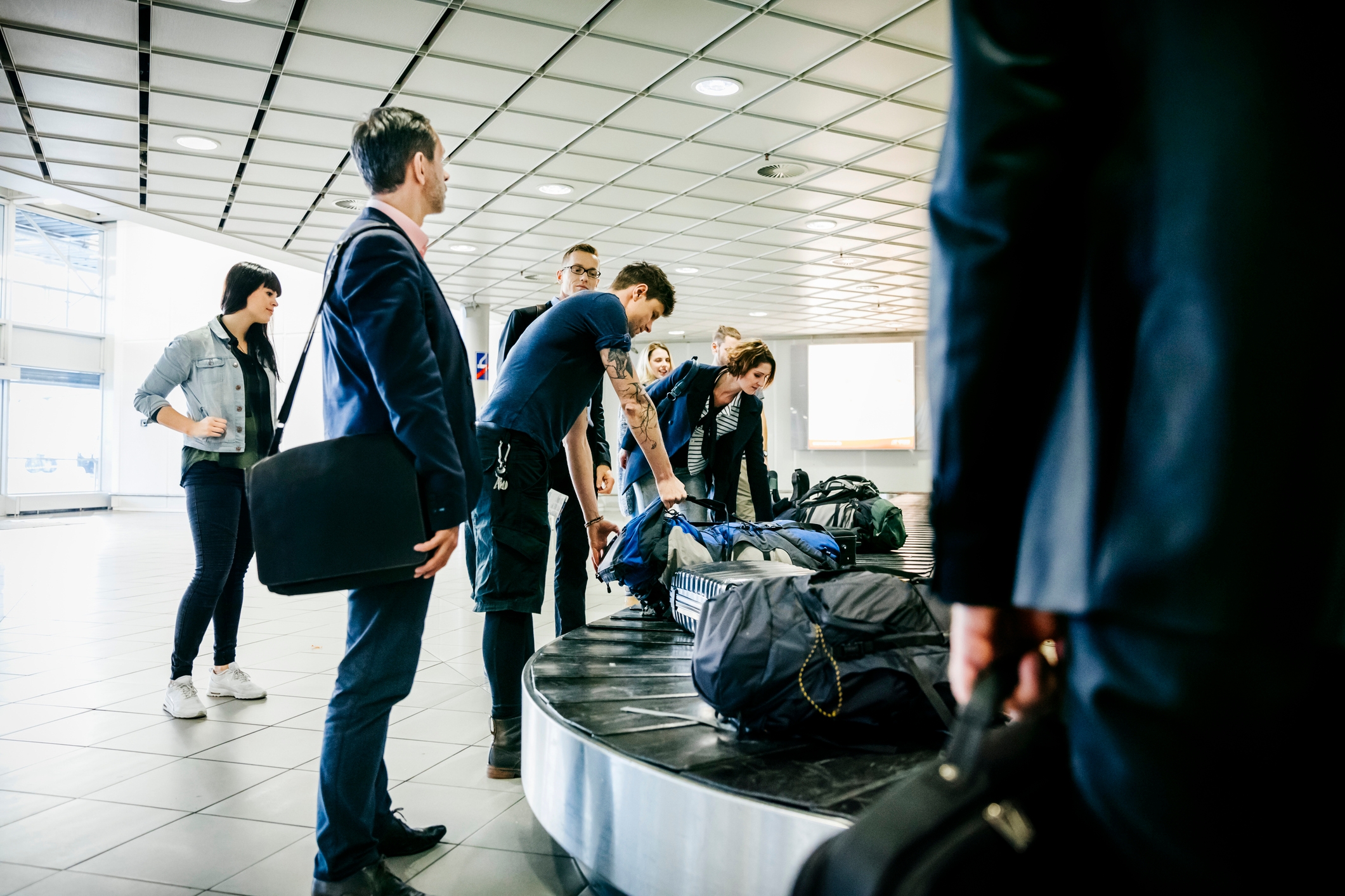 People gather around an airport luggage carousel, retrieving their bags in a busy terminal
