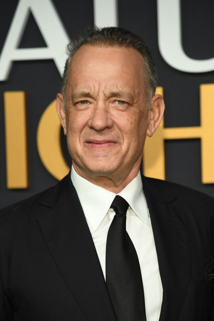 A person in a suit and tie stands on what appears to be a formal event backdrop