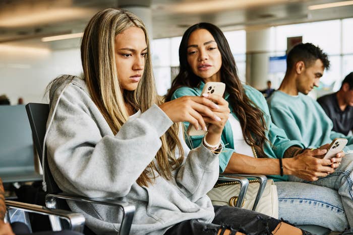 People sitting in an airport lounge, using their phones and waiting. The scene captures a typical travel setting, with travelers engaged in mobile devices
