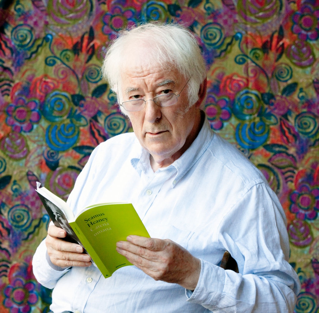 An elderly person in a white shirt reads a book titled &quot;Human Chain&quot; against a vibrant, abstract floral background