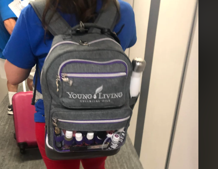Person viewed from behind walking down an airplane aisle with a backpack that contains large bottles and cans