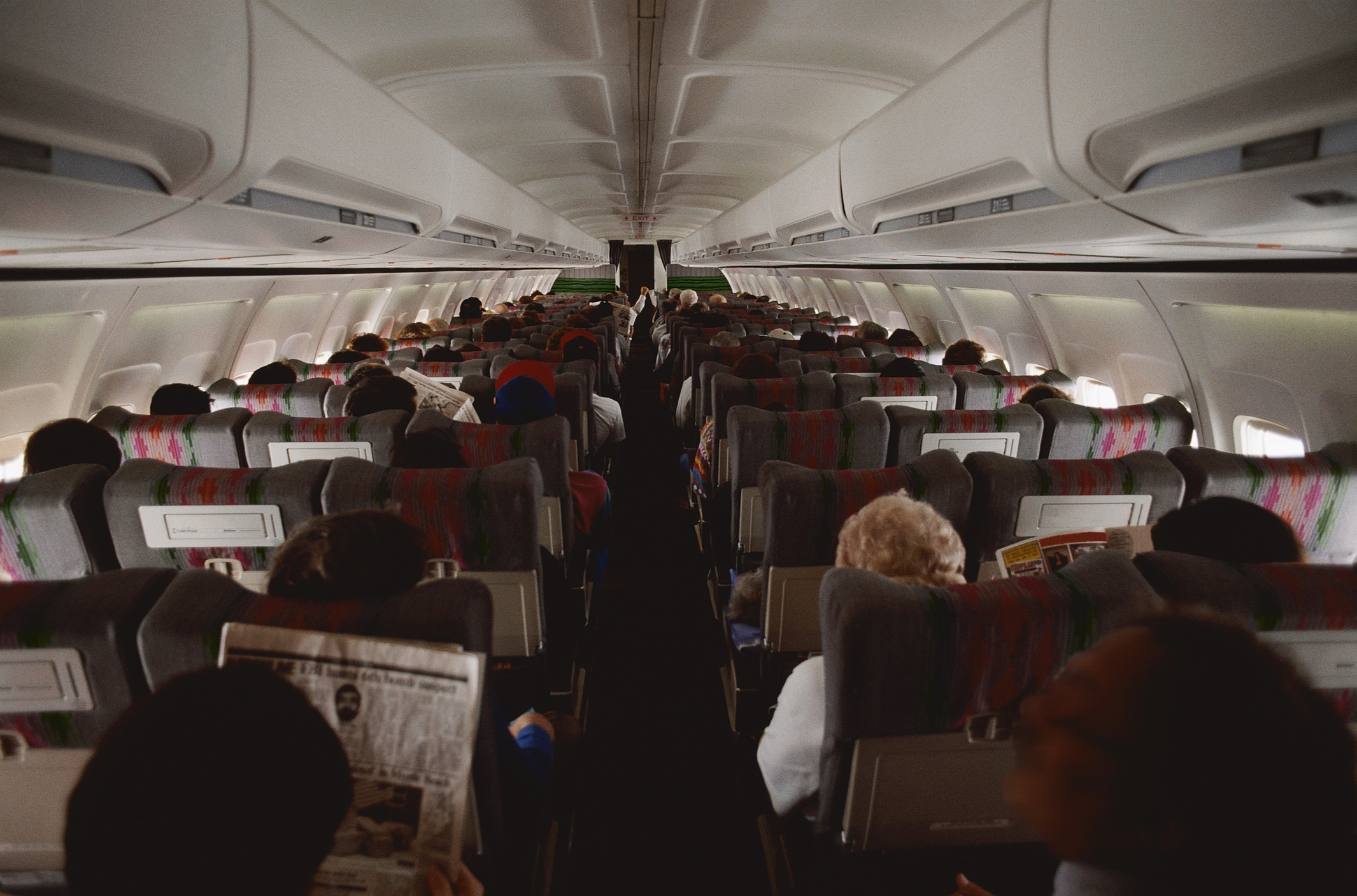 Passengers seated inside a commercial airplane cabin during a flight, with some reading newspapers