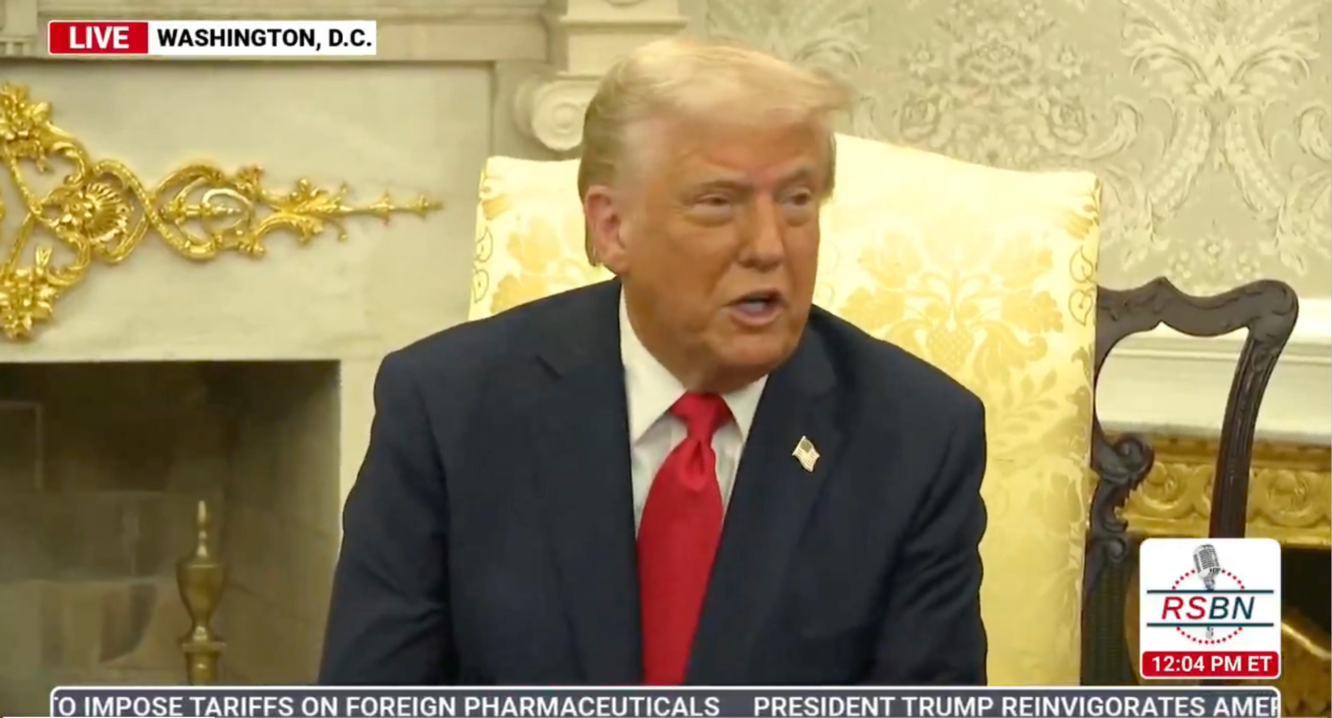 A man in a suit is speaking during a televised event in a formal setting. News ticker mentions tariffs and pharmaceuticals