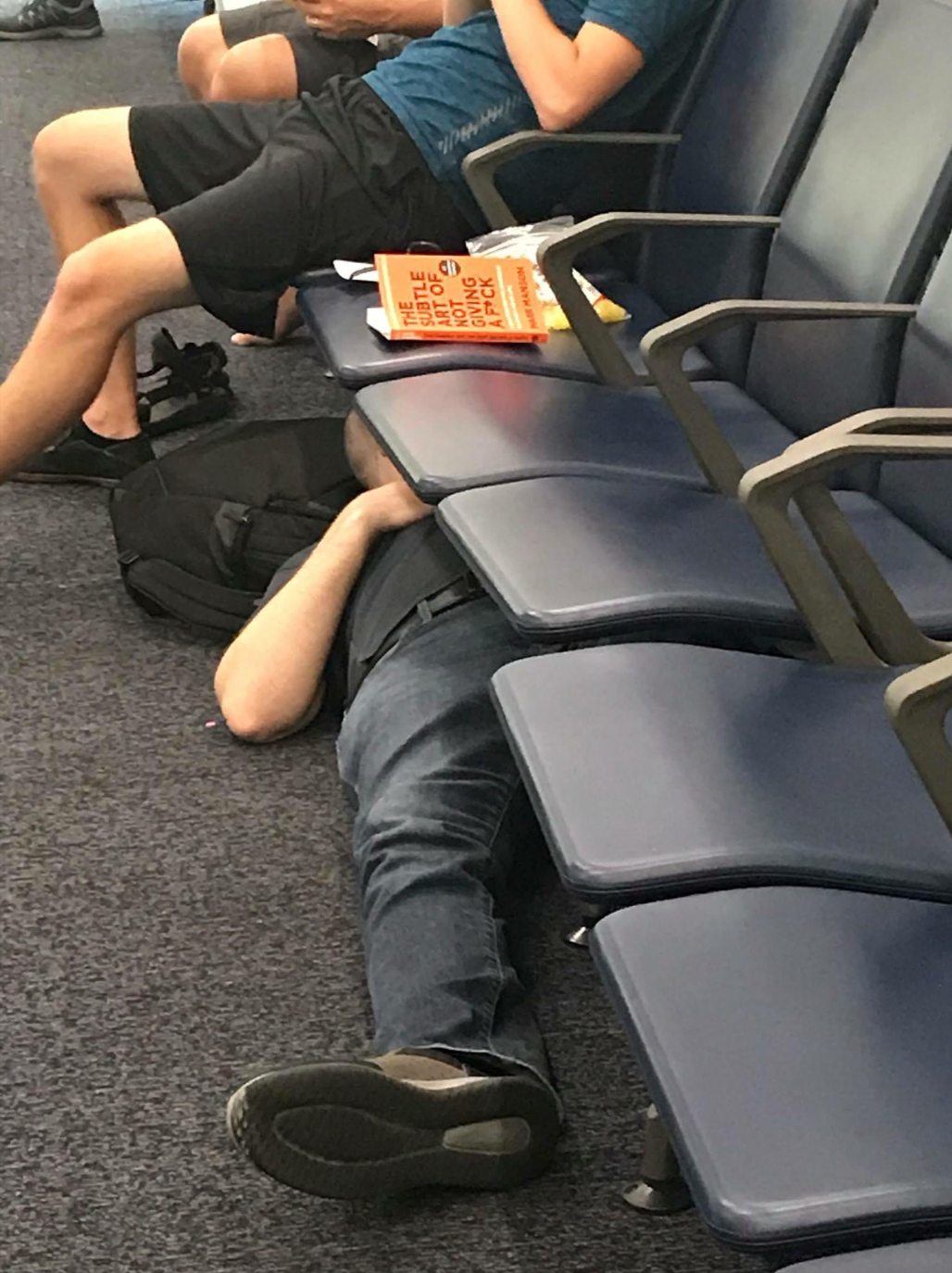 Person lying on floor under airport seats next to a parenting book