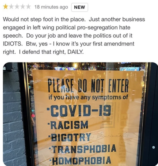 Sign on store window lists symptoms: COVID-19, racism, bigotry, transphobia, homophobia. Reviewer criticizes as political hate speech