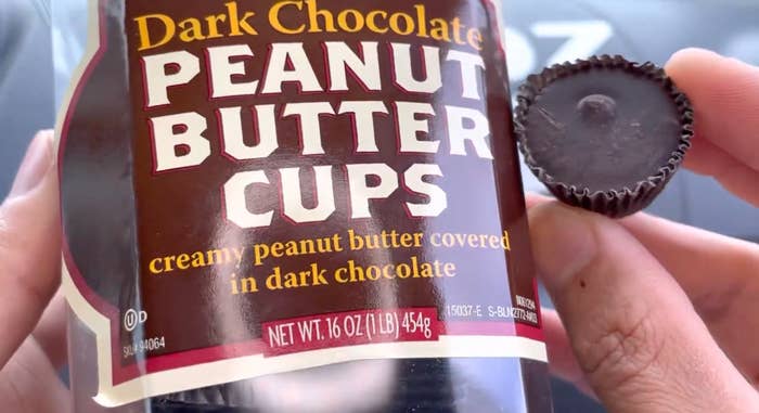 A hand holds a dark chocolate peanut butter cup next to its packaging, labeled "Dark Chocolate Peanut Butter Cups" with serving size details