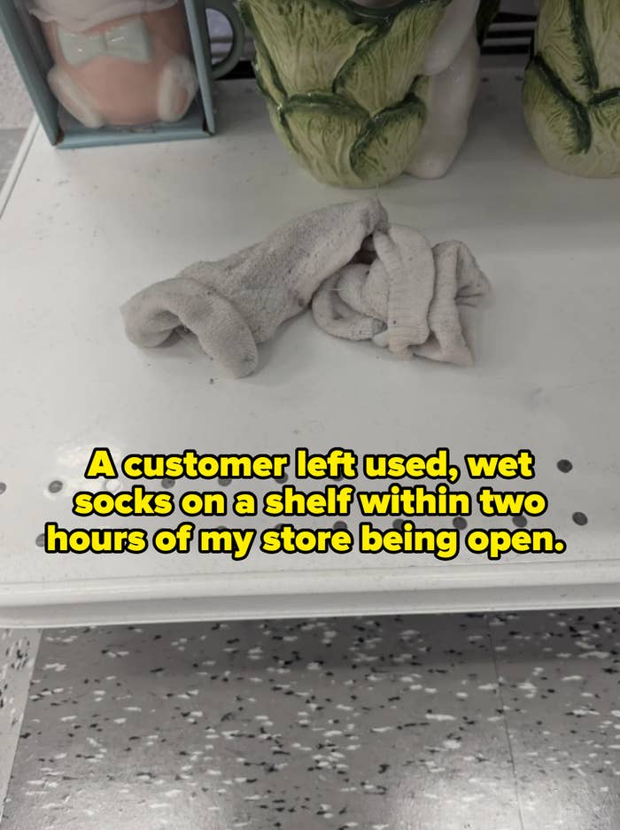 A small grey sock lies crumpled on a white shelf with decorative items in the background