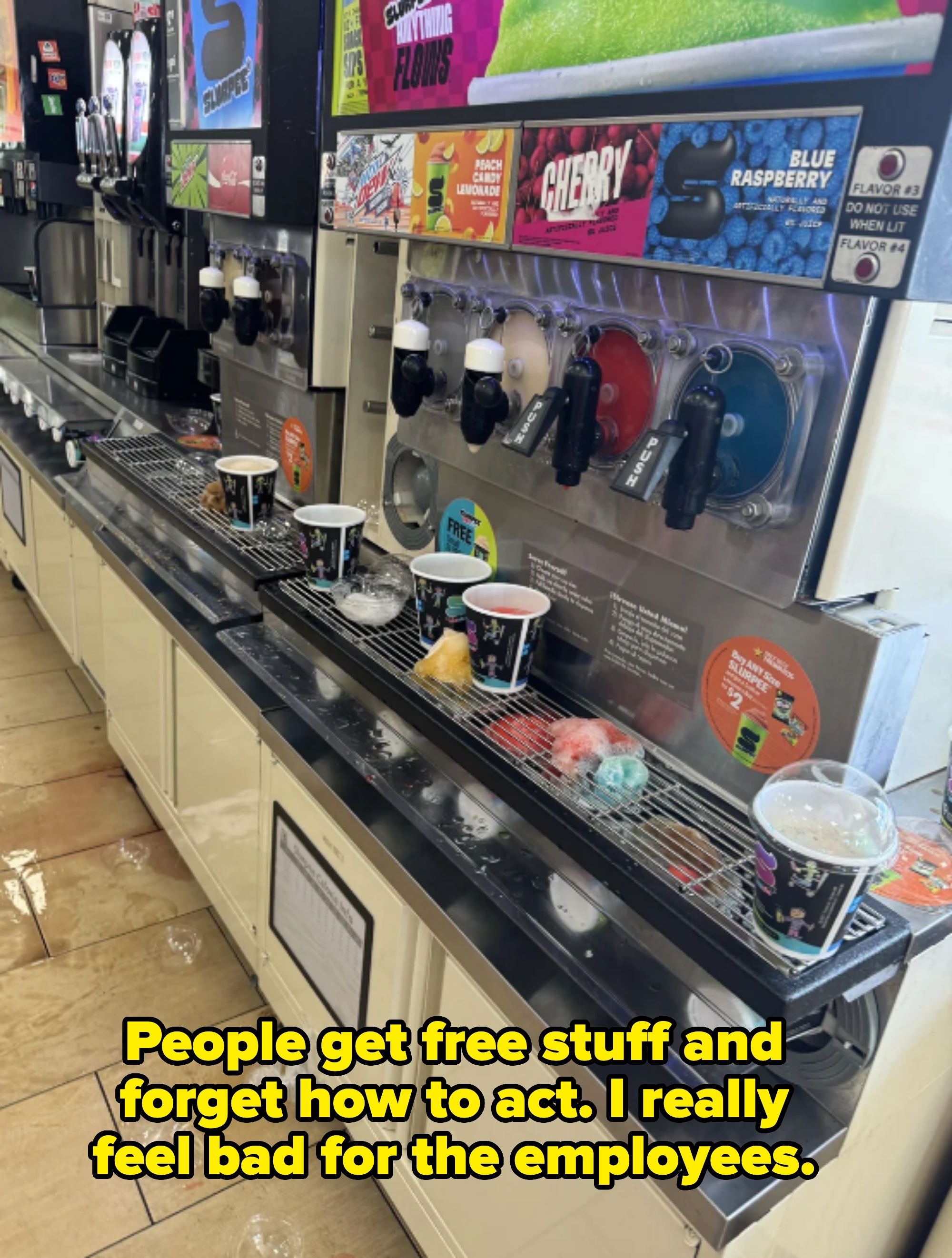 A row of self-serve Slurpee machines with various flavors, cups filled with colorful frozen drinks, and some spills on the counter