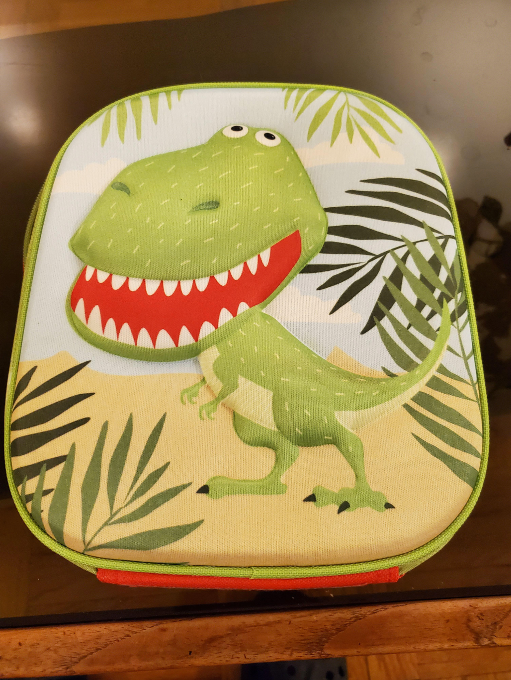 Children's backpack with a cartoon dinosaur design among jungle leaves