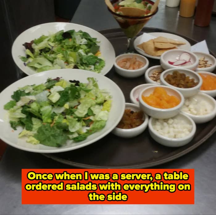 Two plates of leafy salads with a large tray containing small bowls of various toppings, including fruits and vegetables