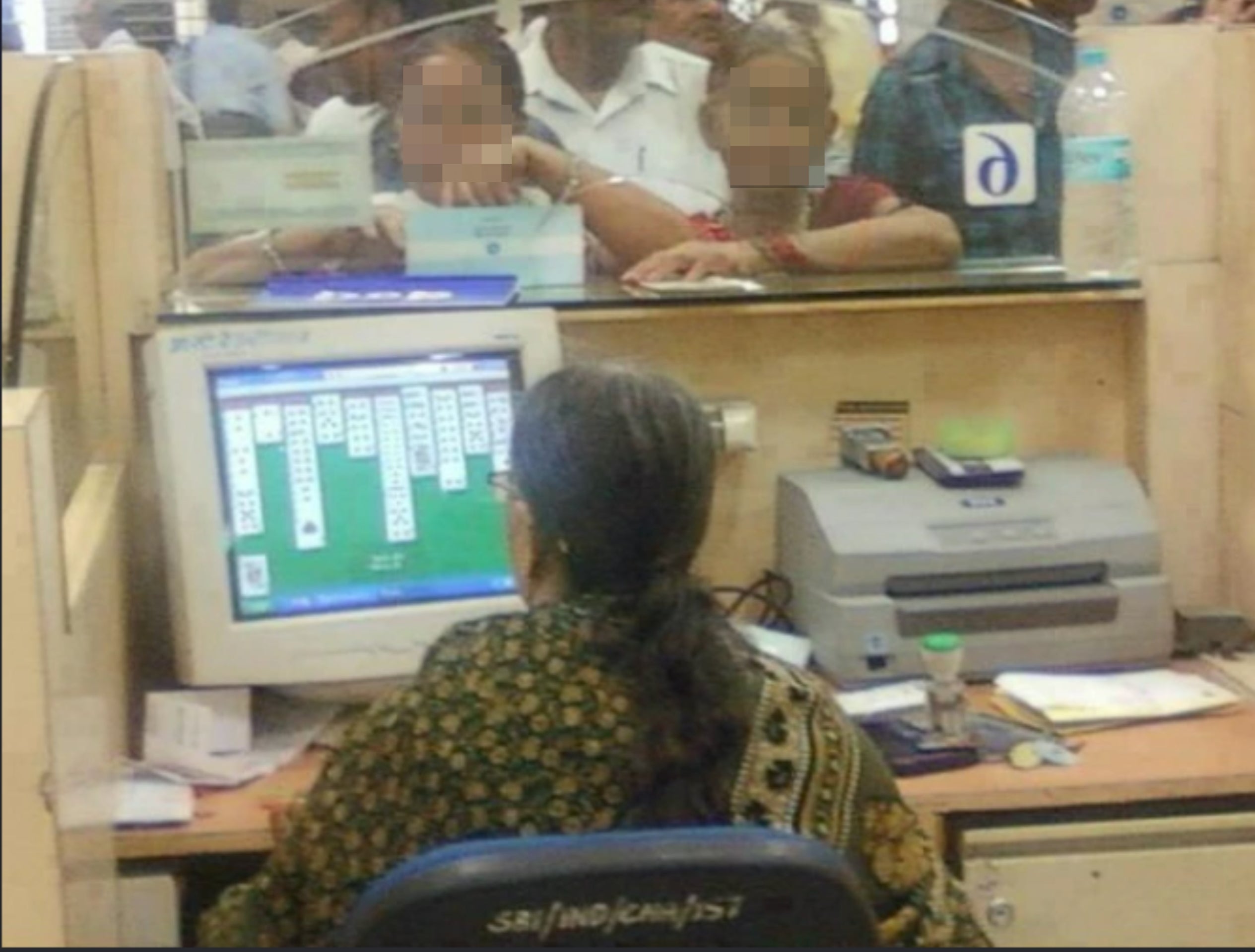 Bank teller plays solitaire on computer while customers wait in line